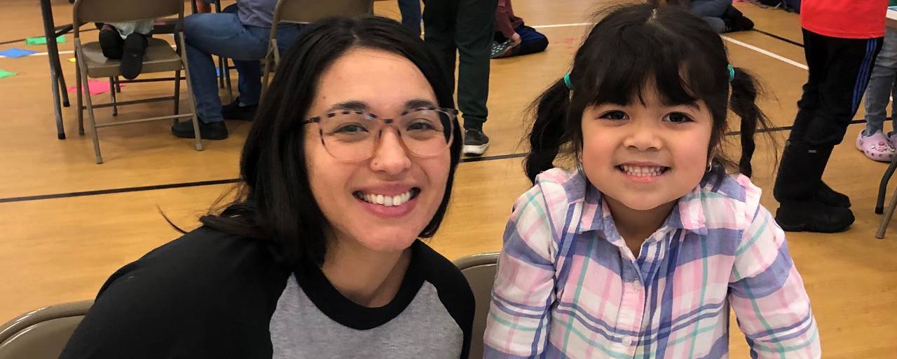 A mom and her young daughter smile at the camera.